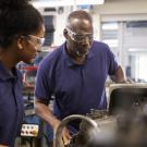 Older African American male mechanic training African American female mechanic in an automotive shop